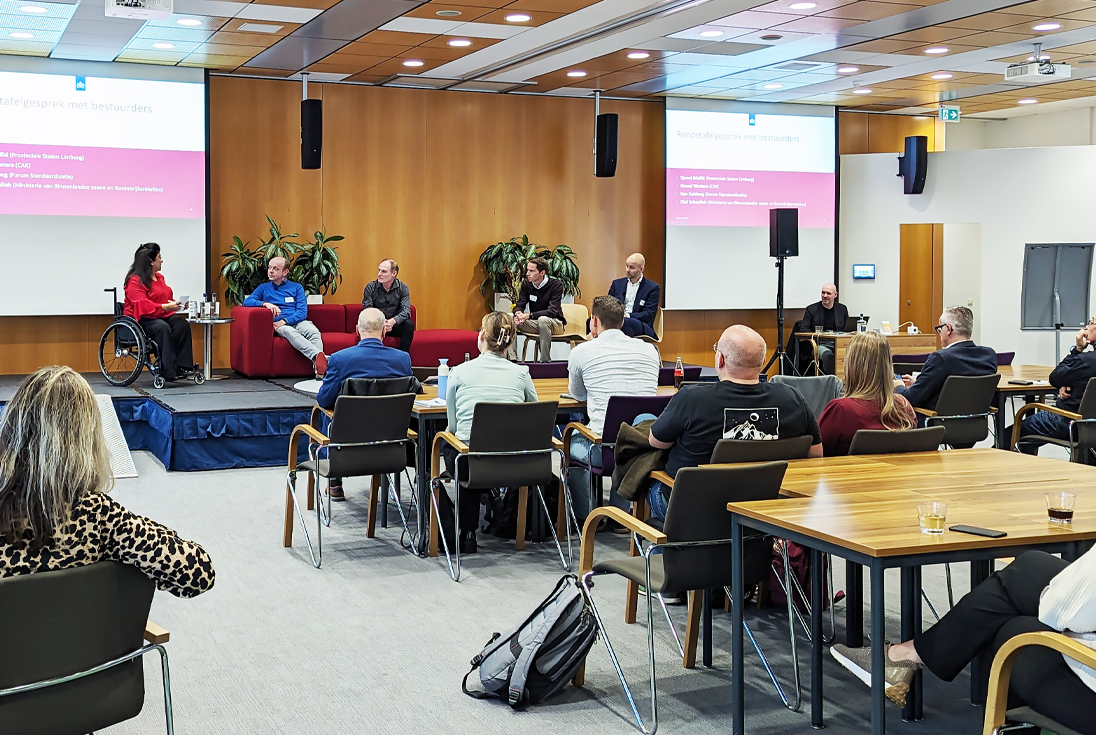 Zaal met op het podium de presentator en bestuurders in gesprek