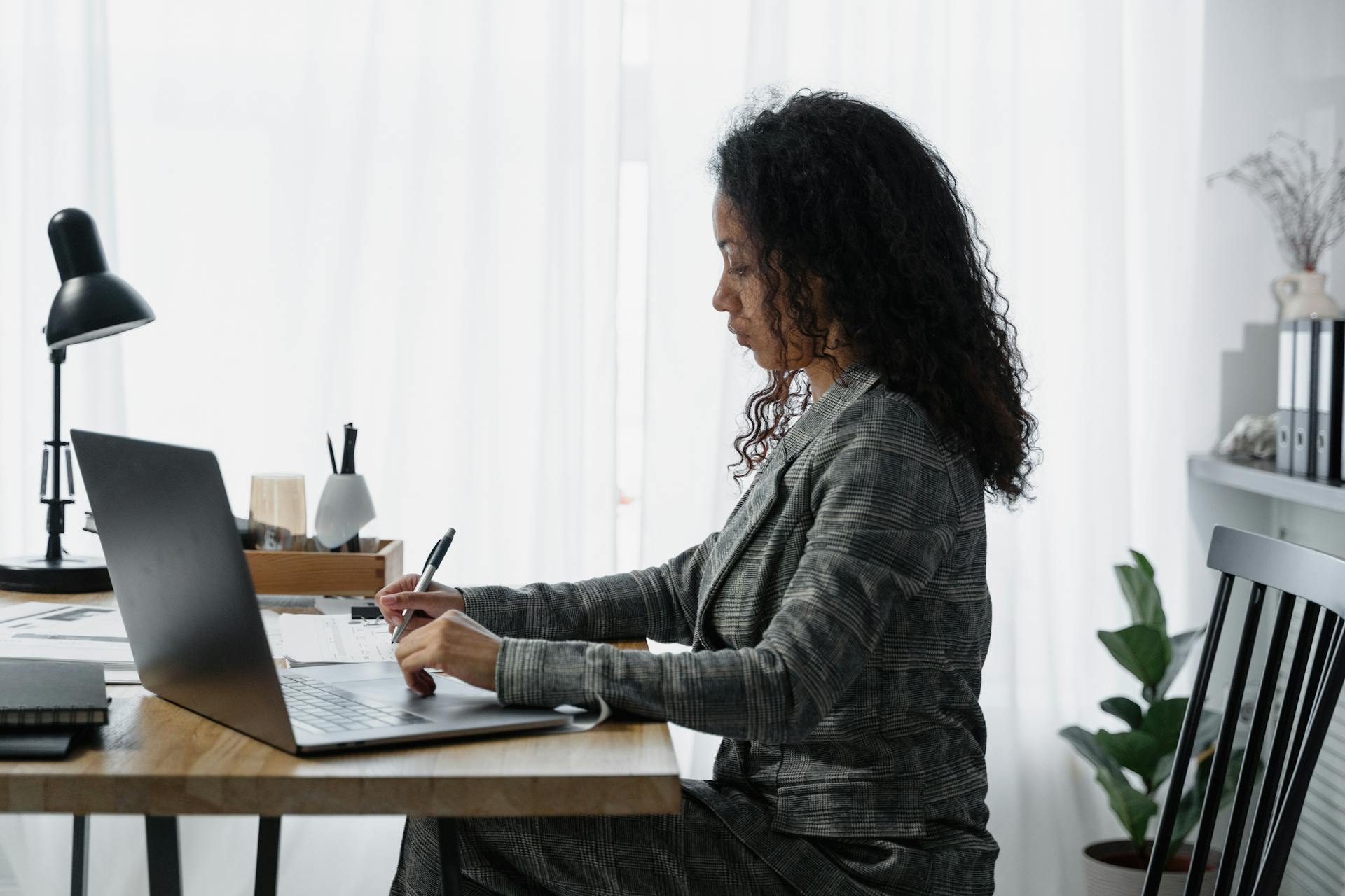 Een vrouw in zakelijke kleding zit aan een bureau achter een laptop en maakt aantekeningen.