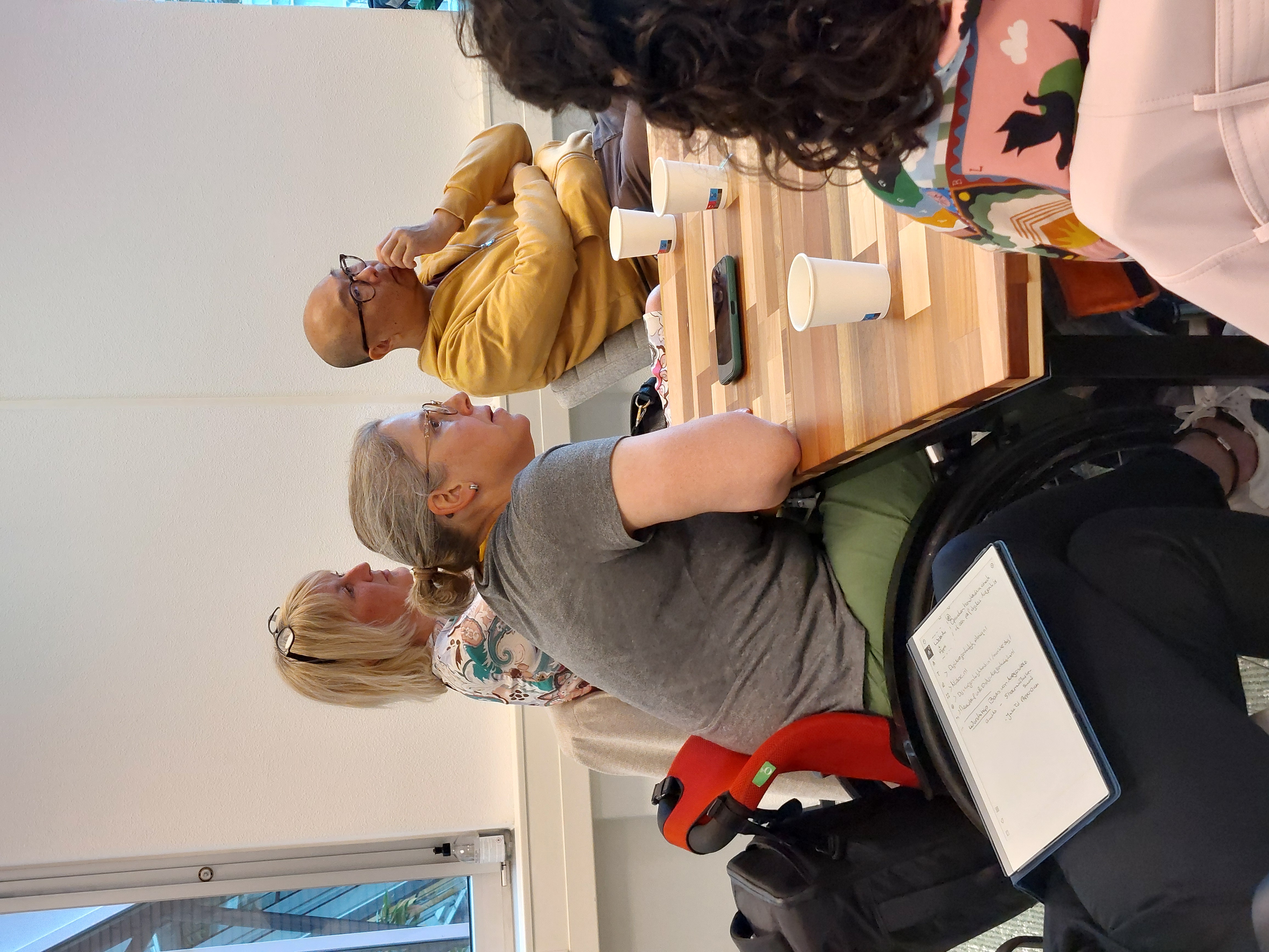 Iemand in een rolstoel zit aan tafel en luistert aandachtig tijdens de workshop