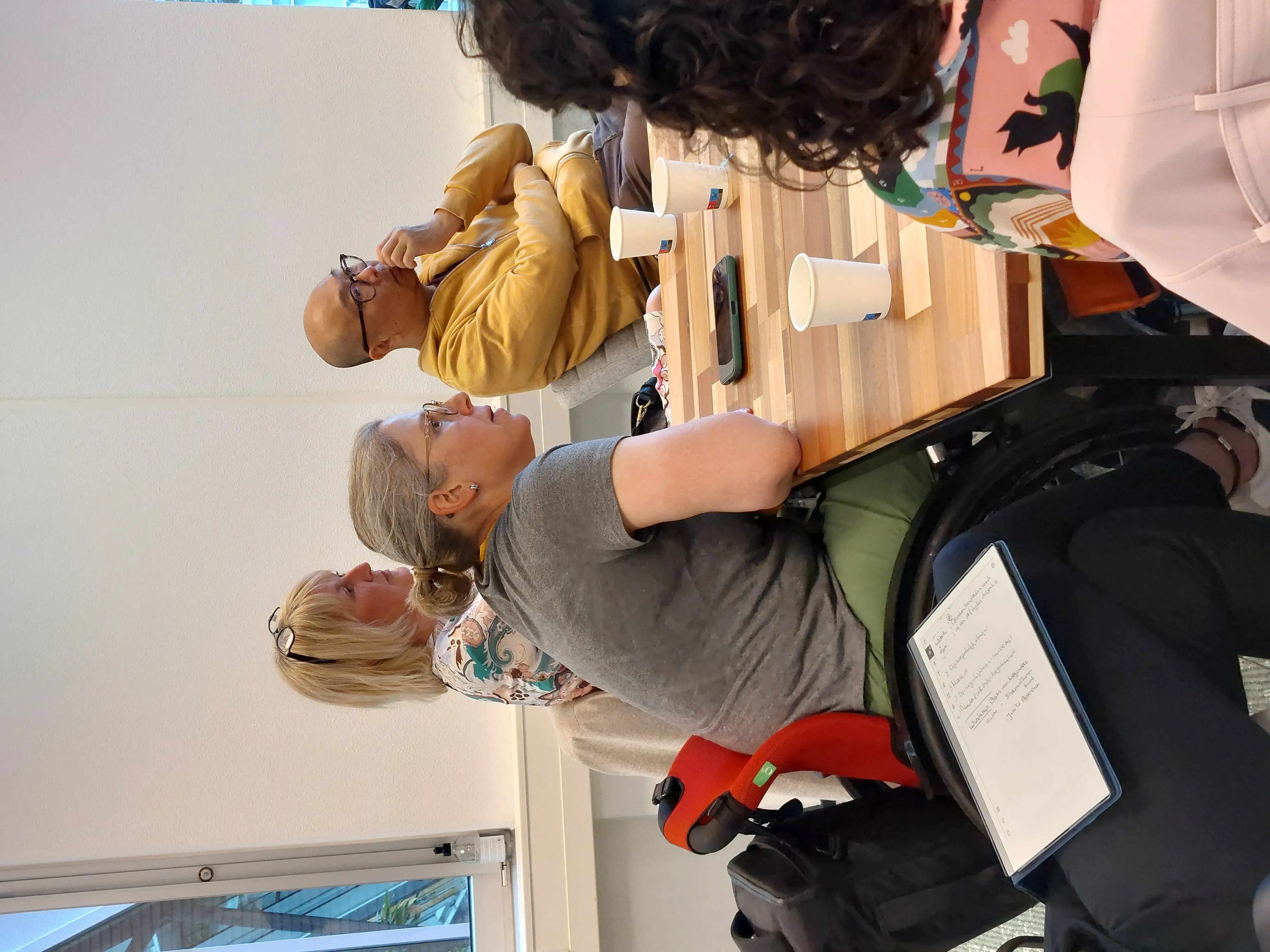 Iemand in een rolstoel zit aan tafel en luistert aandachtig tijdens de workshop