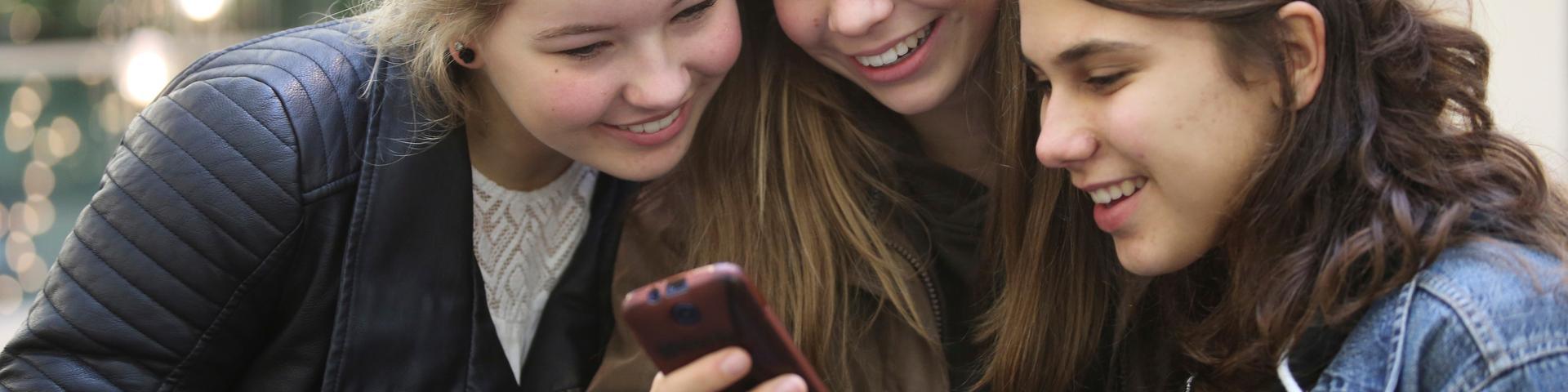 3 meisjes kijken samen naar een mobiele telefoon