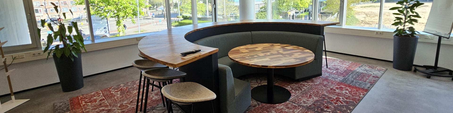 Een workshopruimte bij SVB in Utrecht met een ronde tafel en daaromheen een half ronde bank en een bar met hoge krukken